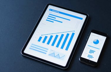 A top-down view of a tablet and a smartphone on a dark blue surface, showing growing bar charts and logistics maps. Modern, tech-focused composition with light blue accents.