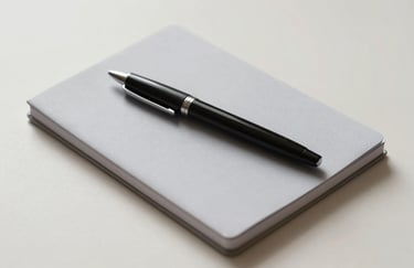Minimalist office supplies including a sleek black pen and a light gray notebook on a pale cream surface, overhead soft lighting.
