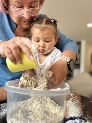 Profe Cris helping a toddler mix flour and water for a textures and cognitive exercise at home.