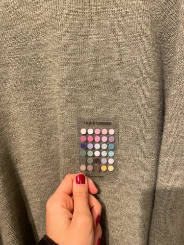 A light summer color palette tool held against a grey knitted sweater for seasonal color analysis.