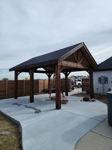 Wooden pavilion with gable roof over concrete pad.