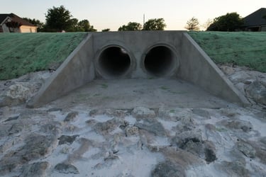 Concrete twin-pipe culvert with rock drainage.