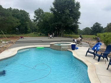 Workers finishing concrete patio near swimming pool and hot tub.