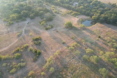 Aerial view of rural land with pond and trees.