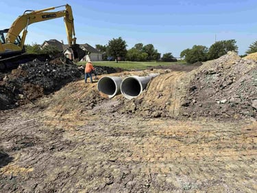Installation of twin concrete drainage pipes with excavator.