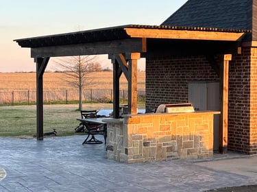 Covered outdoor kitchen with stone bar on stamped concrete patio.
