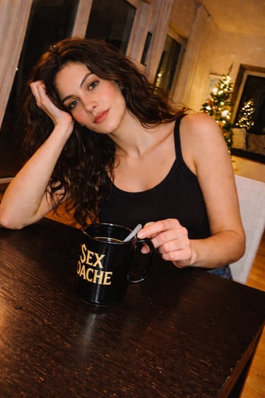 Vera Solina of PreSexHeadache holding a black band mug in a warm personal portrait