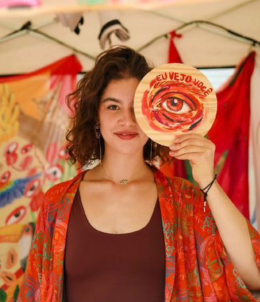 A smiling woman holding a painted wooden disc with an eye illustration over her own eye.