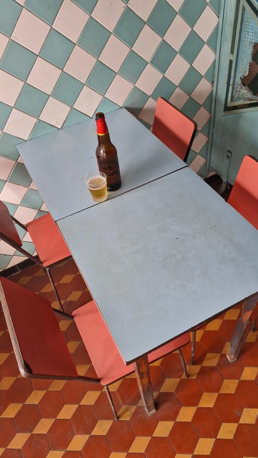 A bottle of beer and a glass on a retro blue table in a diner with checkered tiles.