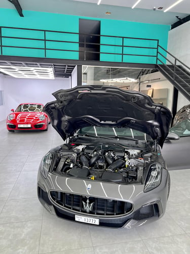 A gray Maserati luxury sports car with its hood open, revealing a powerful engine in a modern showroom.