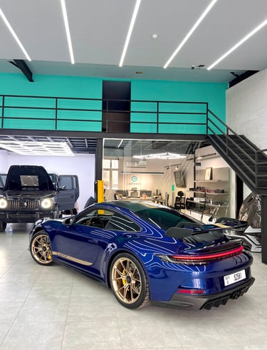 A blue Porsche 911 GT3 with gold wheels parked in a modern luxury car detailing and performance shop.