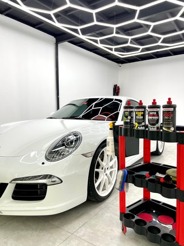 White luxury sports car in a detailing shop with professional polishing compounds on a tool cart.