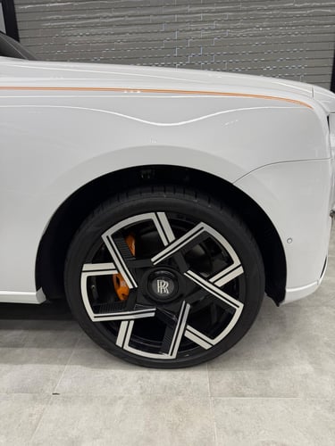 Close-up of a white Rolls-Royce luxury car wheel with custom black and silver rims and orange brake calipers.