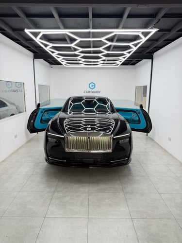 Black Rolls-Royce Spectre luxury electric coupe with blue interior under honeycomb garage lighting.