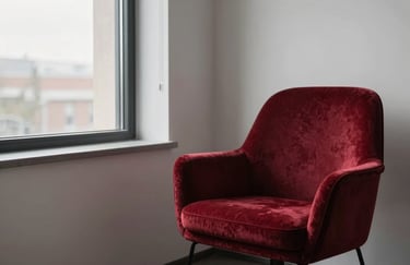 A minimalist agency office corner with a comfortable lounge chair in Deep Ripe Crimson velvet, next to a window with soft morning light.