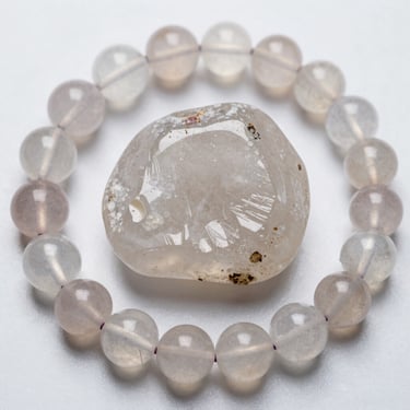 Polished clear quartz crystal stone centered inside a round beaded gemstone bracelet.