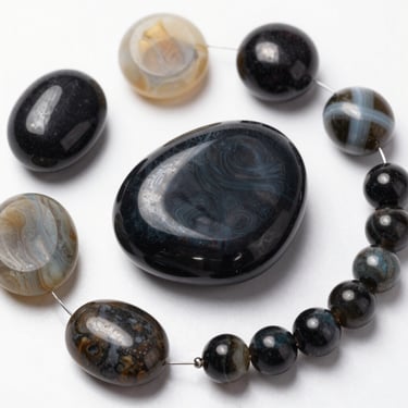 Polished black and grey agate gemstone beads on a string for jewelry making.