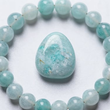 Polished blue amazonite crystal stone surrounded by a beaded gemstone bracelet on a white background.