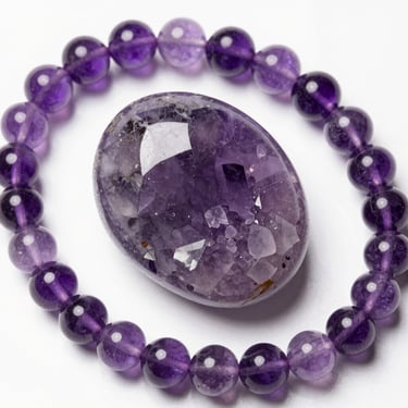 Polished purple amethyst geode crystal surrounded by small faceted amethyst gemstones on a white background.