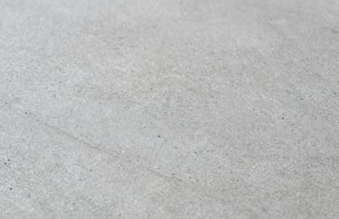 Macro shot of stone-patterned concrete texture, showcasing the fine details and the play of light on the #AEB9B4 surface.