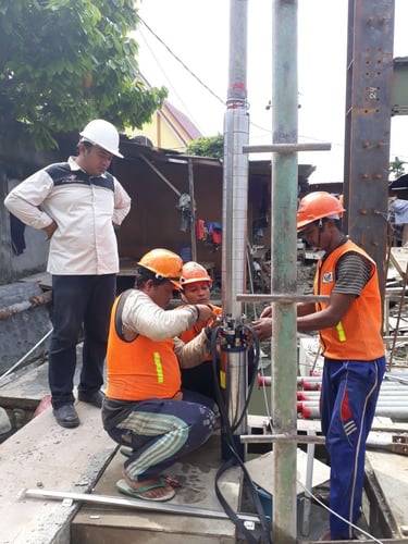 Construction workers in safety gear installing a submersible water pump at an outdoor site.