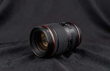 A clean, minimalist photograph of a high-end camera lens resting on a black silk cloth, reflecting soft golden light. Professional photography style in a North American / Global studio context.