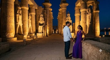 A couple stands amidst the illuminated statues and massive columns of Luxor Temple at night in Egypt.
