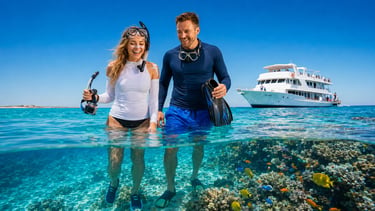 A smiling couple wearing snorkeling gear and rash guards walking through clear blue water over a coral reef.
