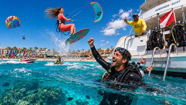 A woman kitesurfing and jumping over a scuba diver near a boat in Hurghada Egypt.