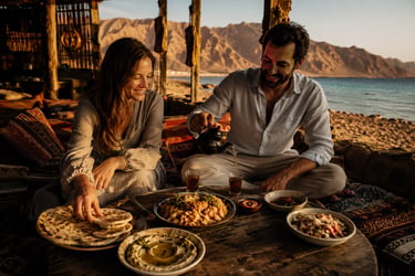 Couple enjoying a traditional middle eastern dinner on a beach at sunset with mountain views.