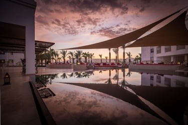 Luxury Hilton Luxor Resort pool reflecting a purple sunset and palm trees under shade sails.