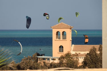 Kitesurfers flying colorful power kites over the blue ocean near a coastal villa tower in El Gouna..