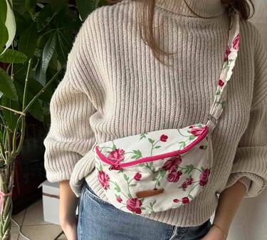 Une femme portant un sac banane à fleurs roses en bandoulière par-dessus un pull à col roulé beige