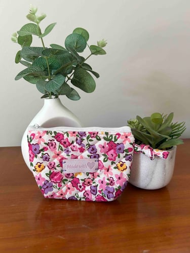 Une pochette matelassée à motif floral rose, confectionnée à la main, posée sur une table en bois.