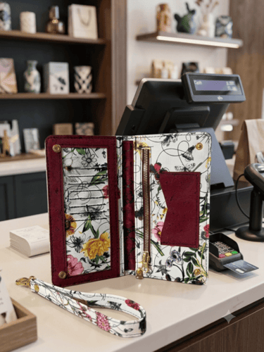 Floral printed leather wallet organizer with wristlet strap on a retail boutique counter.