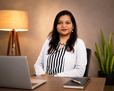 Professional businesswoman in a white blazer sitting at an office desk with a laptop.
