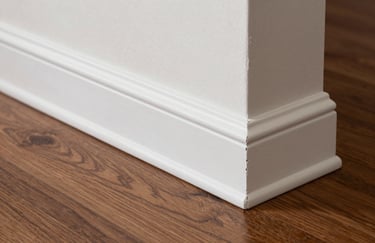 A detailed shot of a perfectly installed white baseboard against a coffee brown laminate floor in a modern South American residence. The focus is on the crisp, clean angle and professional finish.