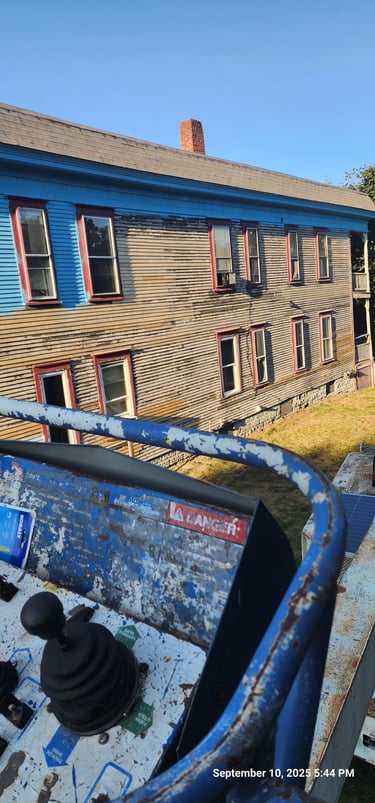 A construction boom lift bucket positioned for exterior painting on a multi-story house siding.
