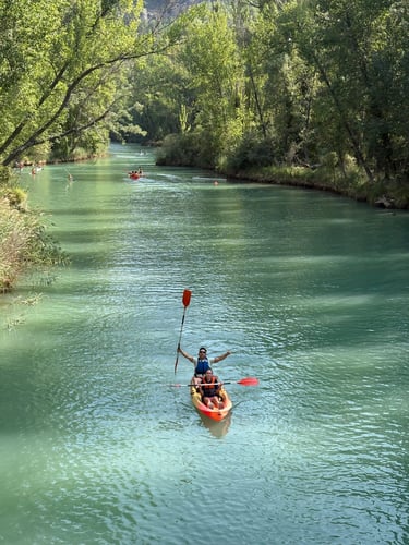 Foto aerea de una pareja en la piragua con los remos en alto y un agua verde preciosa con vegetación
