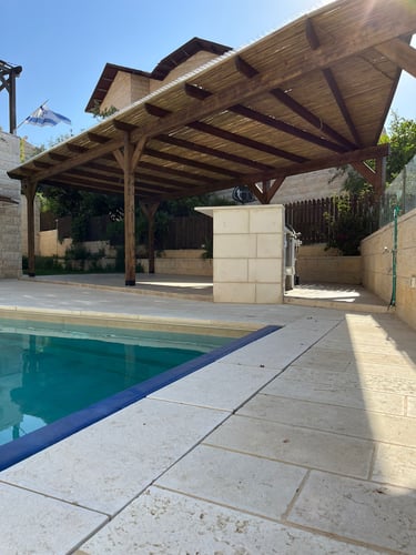 A luxury backyard swimming pool with stone tiling and a wooden pergola for shaded outdoor living.