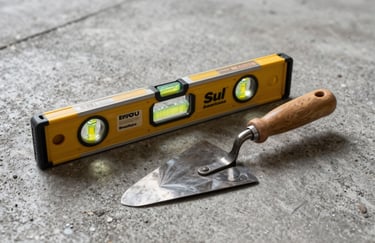 Industrial photography of masonry tools including a spirit level and a metal trowel resting on a grey concrete surface, moody professional lighting, clean composition, Sul Americano / Brasileiro context.