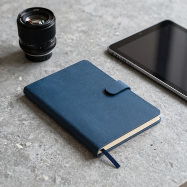 A minimalist photography shot of a clean, modern workspace featuring a steel blue notebook and a sleek tablet on a grey stone desk.
