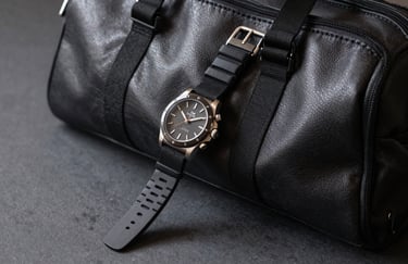 A detailed shot of a luxury watch and athletic wrist wrap resting on a leather gym bag on a dark gray surface, North American professional fitness context.