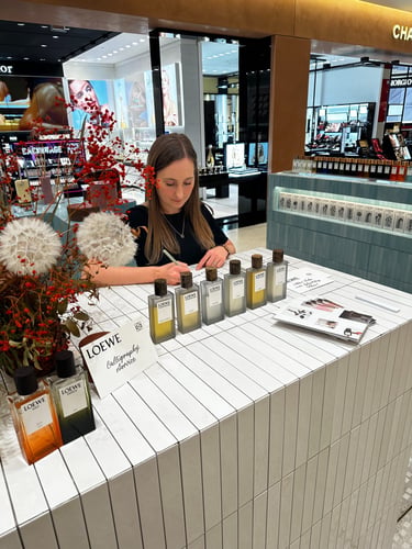 A calligrapher hand-lettering tags at a luxury Loewe perfume counter in a high-end department store.