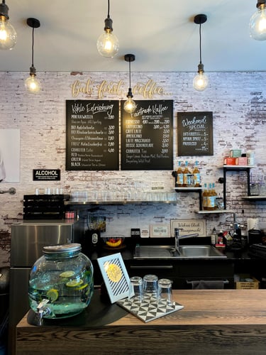 Cozy cafe counter with blackboard menus, hanging Edison bulbs, and a water dispenser with lemon slices.