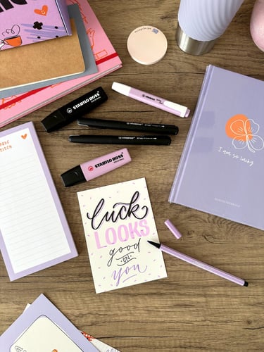 Purple stationery set on a wooden desk with Stabilo Boss highlighters and a hand-lettered card.
