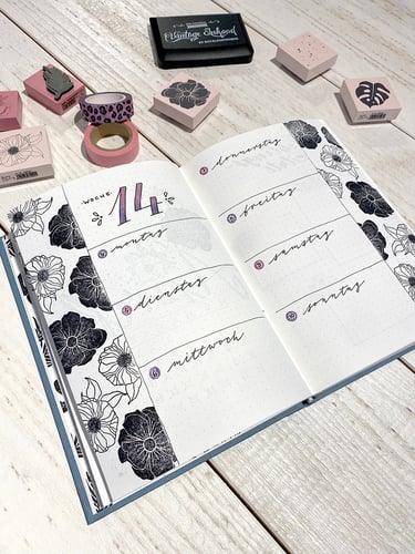 Bullet journal weekly spread with black floral stamps, washi tape, and hand-lettered German days.