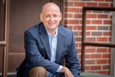 Rene Garcia Corporate Headshot male blue coat blue shirt sitting on stairs with red brick wall 