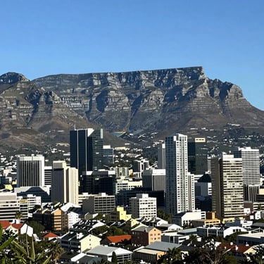 A wide-angle landscape shot of a modern South African urban skyline at dusk, with communication towers subtly visible against a deep blue and teal sky.