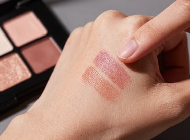 Detail shot of a hand swatching vibrant eyeshadows on skin, professional lighting, feminine aesthetic.